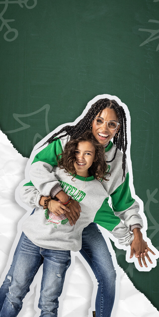A mom and daughter wearing matching grey and green graphic sweatshirt and medium wash jeans.